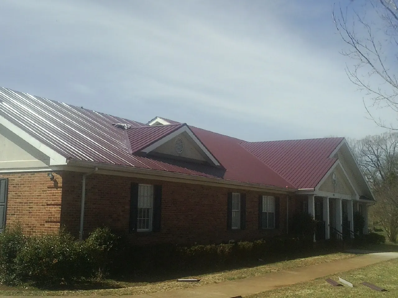 Red metal roof with gabled entries on a long brick building, from a Hail Damage Roof Repair job in Salisbury