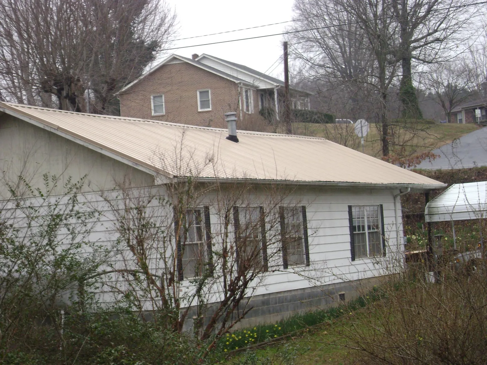 Tan metal roof on a white sided house set into a hillside — Commercial Roofing by Roofing Brothers in Salisbury